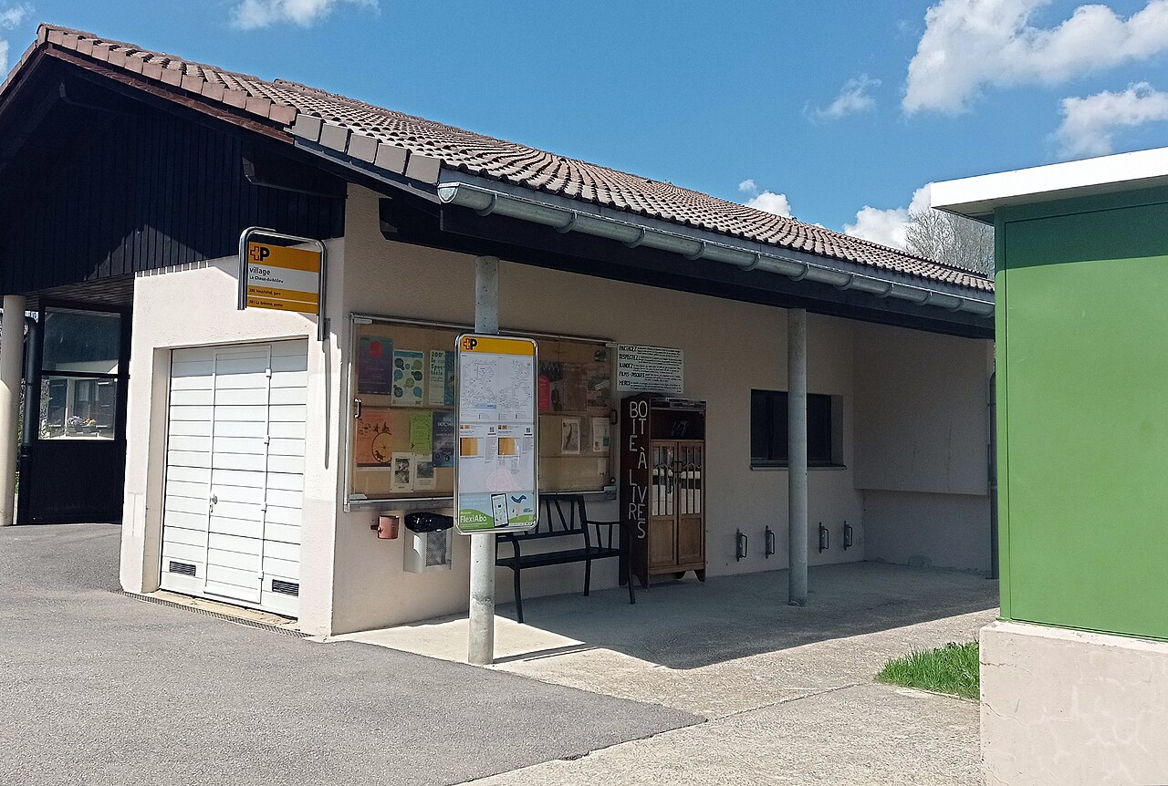 La rue du Centre à La Chaux-du-Milieu, avec un abri-bus et une boîte à livres.