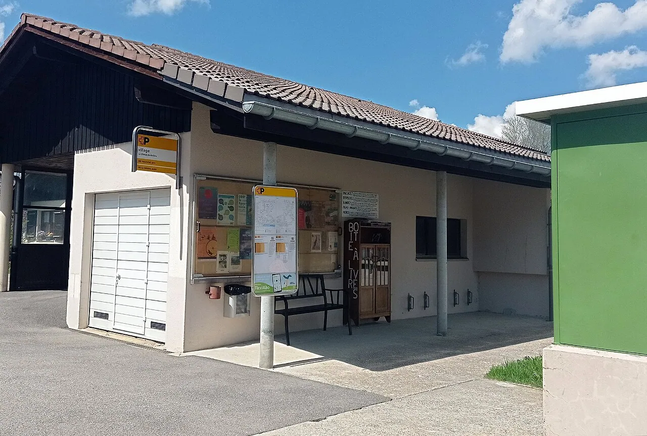 La rue du Centre à La Chaux-du-Milieu, avec un abri-bus et une boîte à livres.